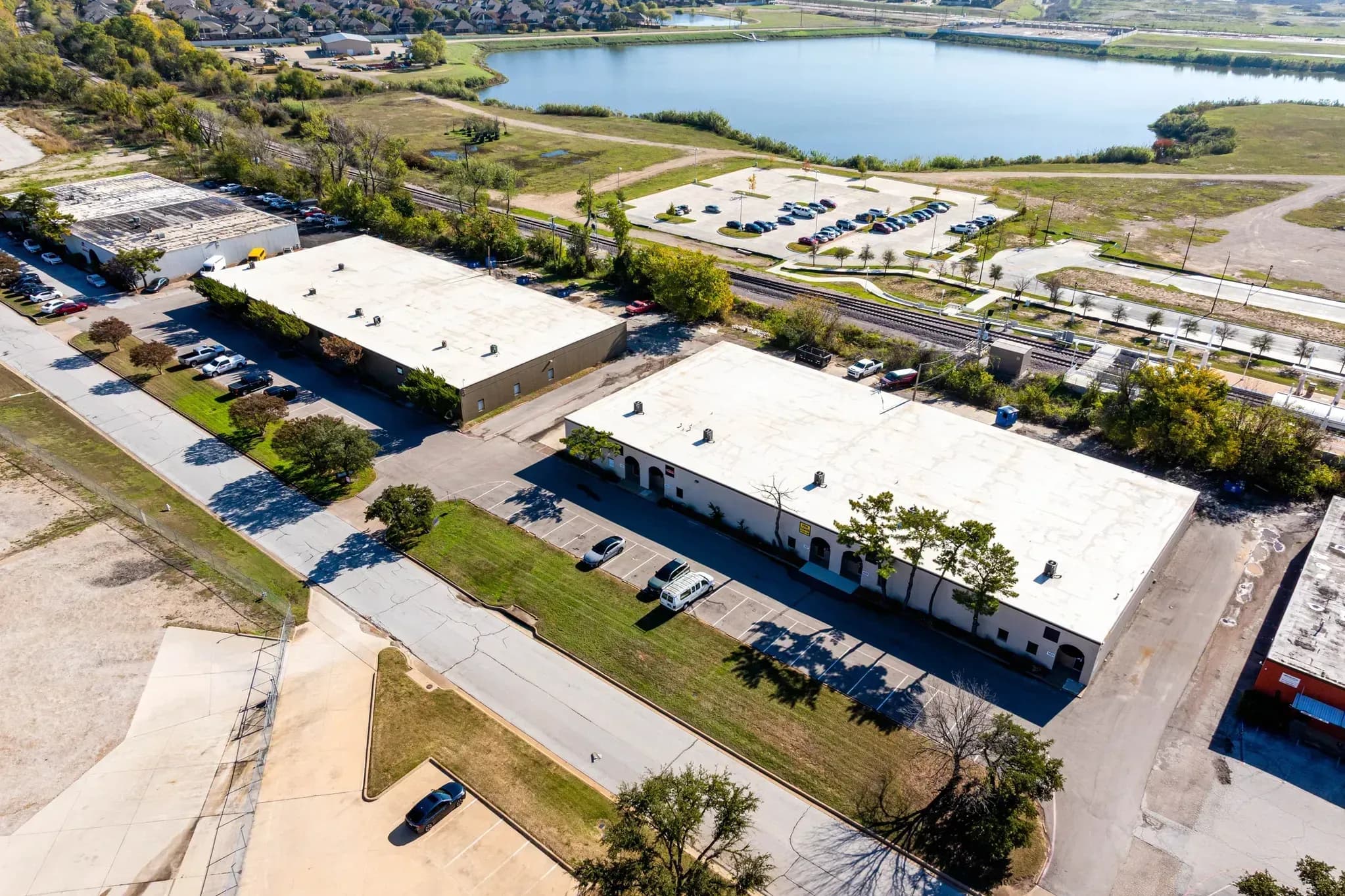 Aerial view of industrial warehouse buildings with parking lots near a waterway and green fields.