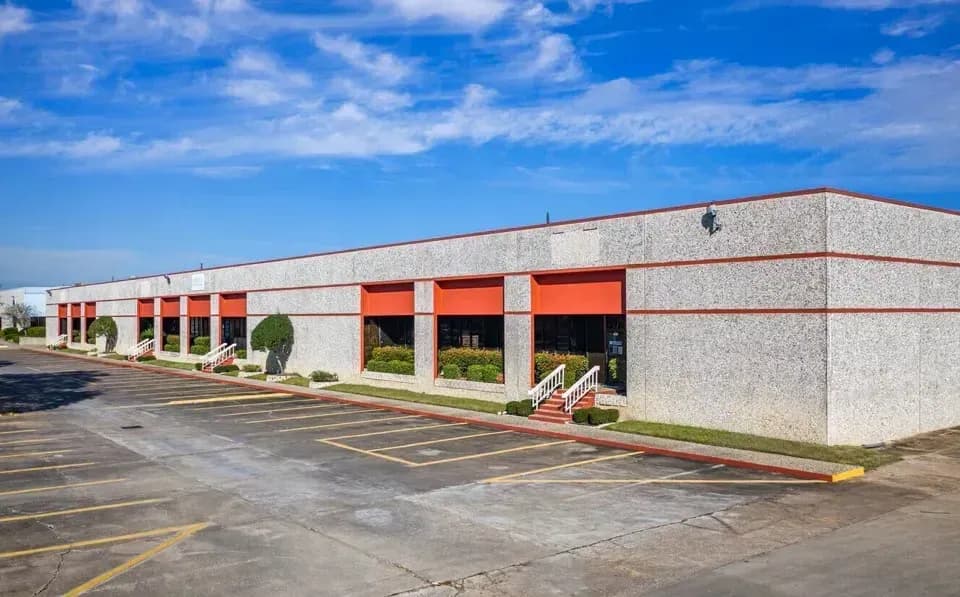 Commercial building with red overhead doors, concrete facade, and parking lot under blue sky